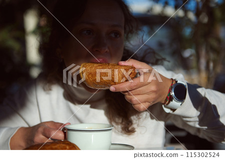 Woman enjoying a croissant and coffee during breakfast in a cozy cafe 115302524