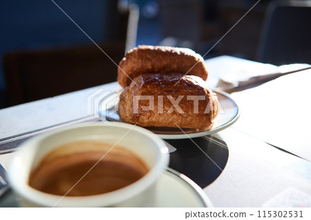 Fresh croissants and a steaming cup of coffee on a sunlit morning table Fresh croissants and a steaming cup of coffee on a sunlit morning table 115302531