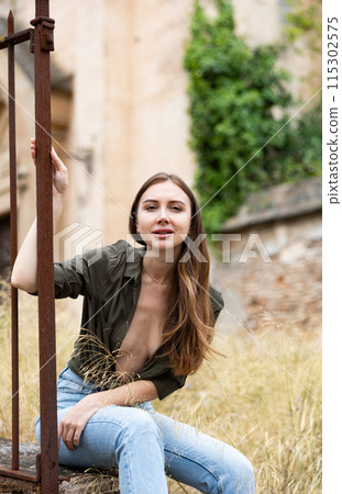 Woman in unbuttoned blouse posing near fence Woman in unbuttoned blouse posing near fence 115302575