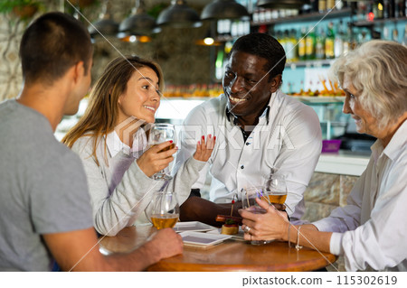 Happy men and women friends enjoy and fun holiday party with glasses of beer. Focus on african american man 115302619