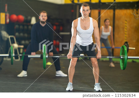 Sportive young man lifting barbell in sports hall 115302634