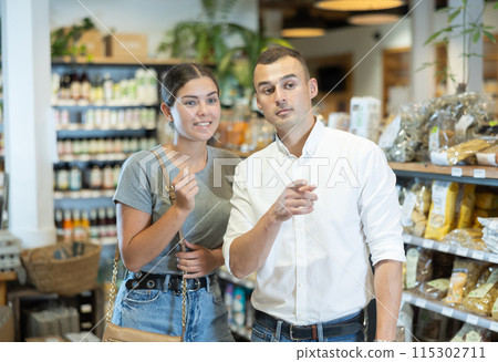 Positive young couple looking around standing by food-shelves in supermarket 115302711