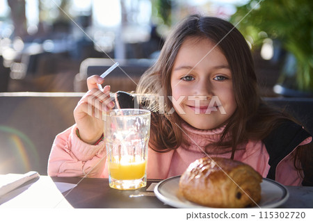 Smiling girl enjoying breakfast with orange juice and pastry at outdoor cafe 115302720