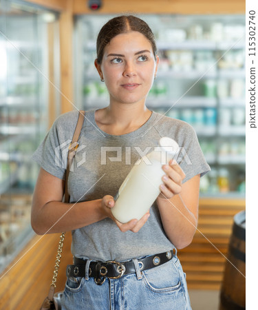 Young woman in supermarket buys bottle of milk Young woman in supermarket buys bottle of milk 115302740
