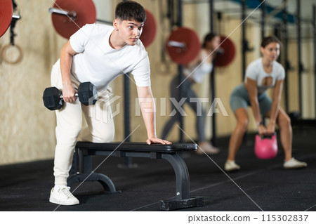 Young guy training with dumbbells on bench Young guy training with dumbbells on bench 115302837