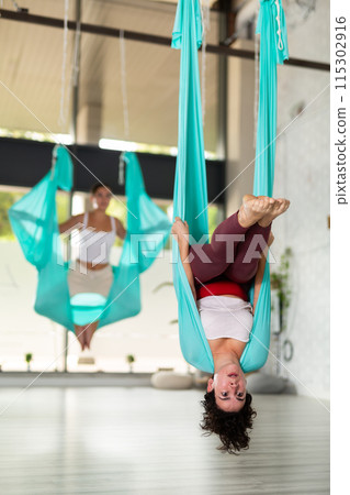 Active young Latin female performing Aerial yoga exercise or antigravity yoga indoor. Pilates, stretch, balance, healthy lifestyle 115302916