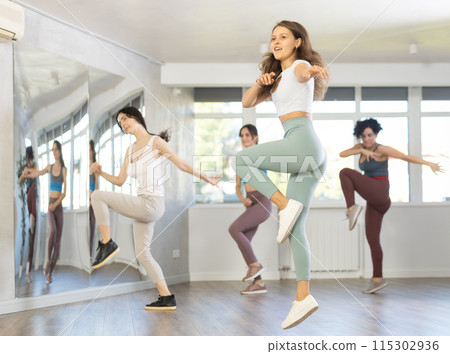 Women perform choreographic exercises energetic dance together. Hip hop in spacious training hall Women perform choreographic exercises energetic dance together. Hip hop in spacious training hall 115302936