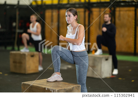 Motivated girl performing step-ups on plyo box during group workout 115302941