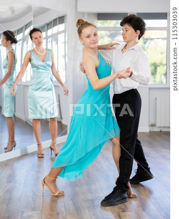 Girl and a boy in festive clothes learn to dance tango under guidance of teacher Girl and a boy in festive clothes learn to dance tango under guidance of teacher 115303039