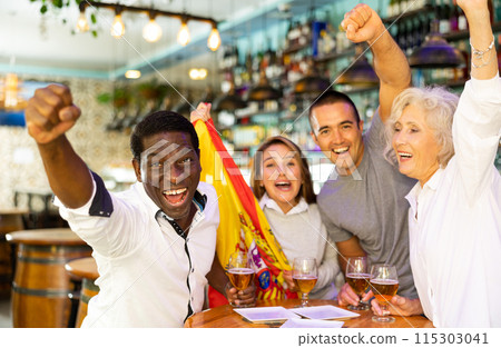 Cheerful international sport football fans waving Spanish flag and drinking beer in the sport bar Cheerful international sport football fans waving Spanish flag and drinking beer in the sport bar 115303041