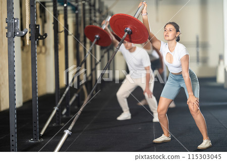 Athletic young woman pumping up her arm biceps using one side of barbell 115303045
