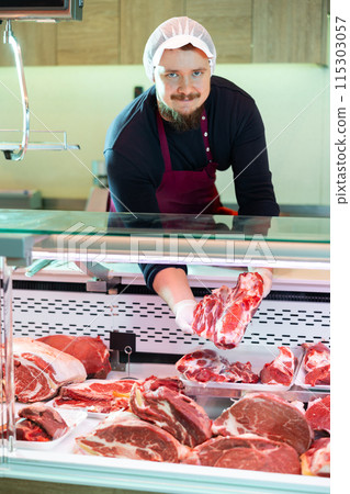 Male butcher putting raw meat on supermarket display Male butcher putting raw meat on supermarket display 115303057