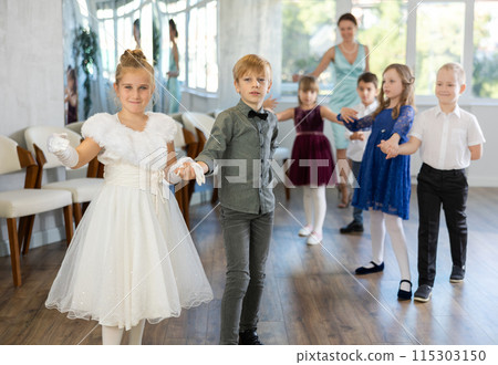 Little children in elegant dresses standing in pairs in dance pose in school hall 115303150