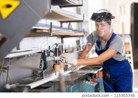 Smiling female technician operating profile cutting machine in workshop Smiling female technician operating profile cutting machine in workshop 115303398