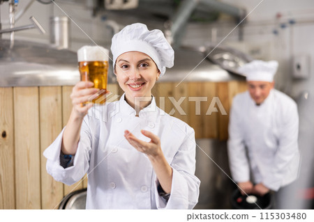 Successful female brewmaster holding glass of foamy ale 115303480