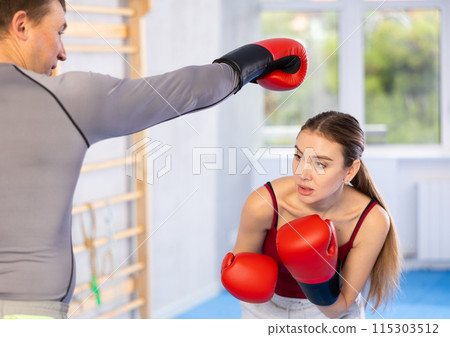Young girl training boxing kicks on punch mitts held by male instructor 115303512