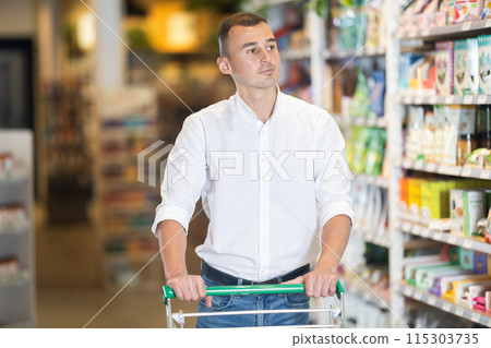 Male shopper with trolley in trading floor browses eco product in bio shop search perfect goods 115303735