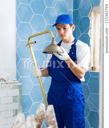 Focused young plumber installing shower in apartment under renovation 115303769