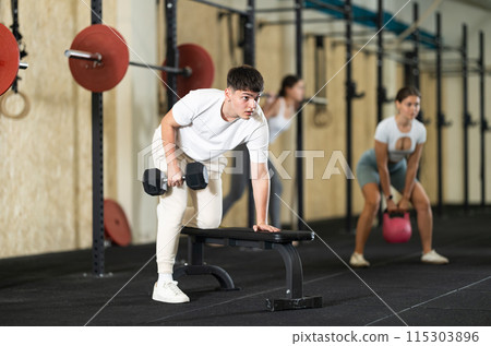 Young guy training with dumbbells on bench Young guy training with dumbbells on bench 115303896