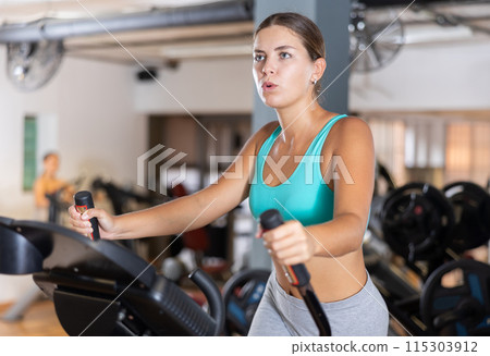 Young woman working out on elliptical machine 115303912