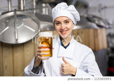 Female brewer showing thumbs up while holding glass of beer 115303955