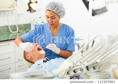 Focused woman dentist treats a man patient 115303961