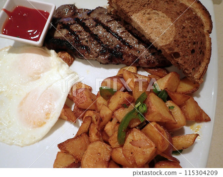 Steak with two eggs over easy, two slices of rye bread, potatos and cup of ketchup Steak with two eggs over easy, two slices of rye bread, potatos and cup of ketchup 115304209