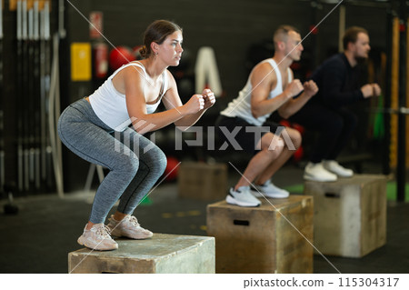 Sportive young girl squatting on box during crossfit workout Sportive young girl squatting on box during crossfit workout 115304317