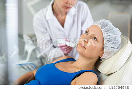 Woman getting facial radio wave lifting skin tightening procedure in salon. RF-lifting device treatment of acne scars, cellulite, skin rejuvenation, Concept of professional cosmetology and 115304428