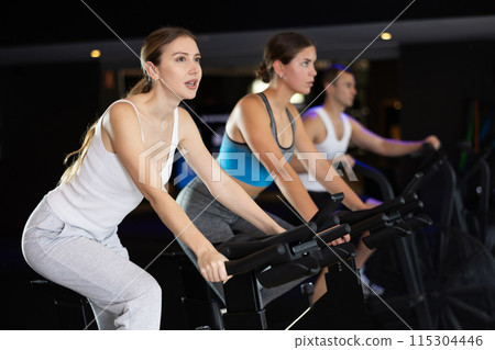 Girl performs exercises with stationary bicycle in gym Girl performs exercises with stationary bicycle in gym 115304446