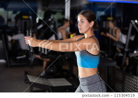 Active athlete young woman during exercises on crossover exercise machine with loops and weighting Active athlete young woman during exercises on crossover exercise machine with loops and weighting 115304519
