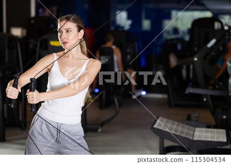 Active athlete young woman during exercises on crossover exercise machine with loops and weighting 115304534