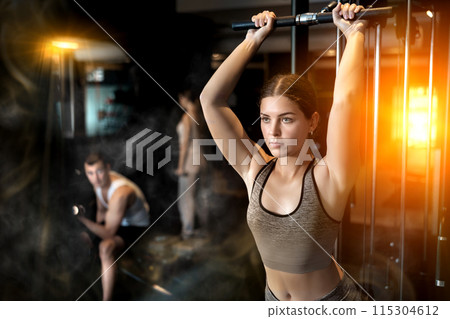 Slender athletic girl work out muscles of arms and shoulders on simulator in gym of fitness club Slender athletic girl work out muscles of arms and shoulders on simulator in gym of fitness club 115304612