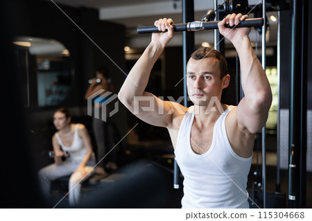 Sportive young guy training on cable exercise machine in gym 115304668