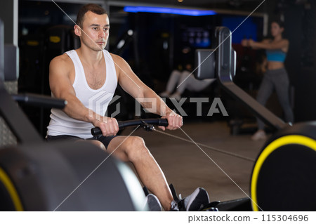 Sportive young guy training on cable row machine in gym 115304696