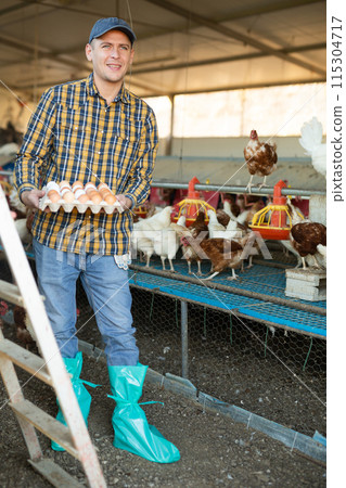Portrait of man farmer holding eggs in hands in henhouse 115304717