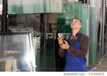 Male worker using control panel and lifting mechanism controls movement of window panes in an industrial workshop 115304872
