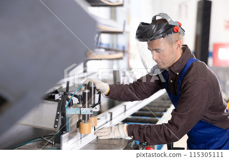 Glass workshop - man works on machine for cutting aluminum profiles for windows 115305111