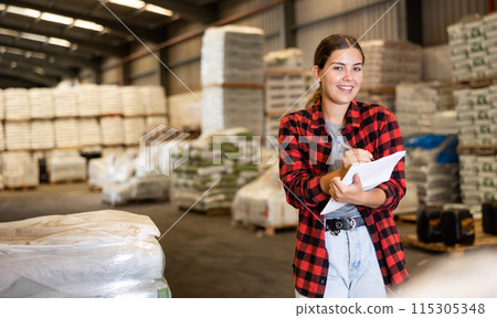Female manager leads the accounting of materials in large warehouse 115305348