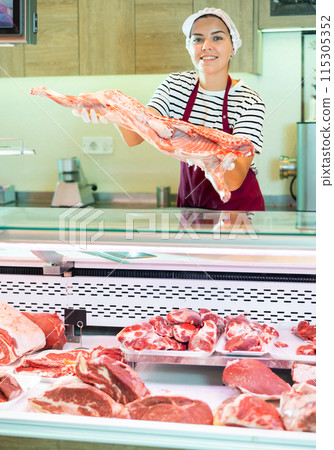 Young female butcher putting raw meat on supermarket display Young female butcher putting raw meat on supermarket display 115305352