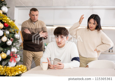 Quarrel during Christmas celebration - father and sister scolding young guy in home kitchen 115305361