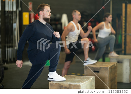 Sportive young guy doing step-up exercises with box during crossfit workout 115305362