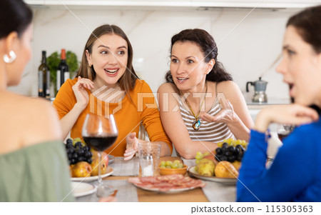 Girlfriends drinking wine and having conversation over dinner at house party 115305363