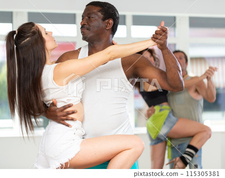 Smiling multiracial men and women enjoying partner dance while training together in studio 115305381