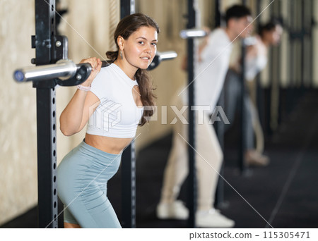 Girl in activewear exercising with barbell during group workout in gym center 115305471