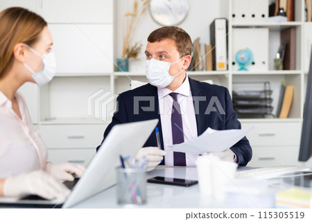 Entrepreneur in medical mask working with female coworker in office Entrepreneur in medical mask working with female coworker in office 115305519
