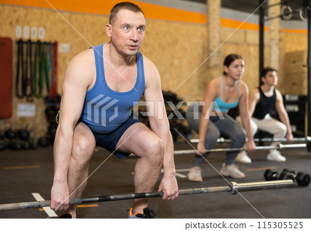 Man exercising with barbell during intense group workout 115305525