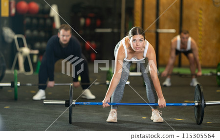 Sportive young woman lifting barbell in sports hall 115305564