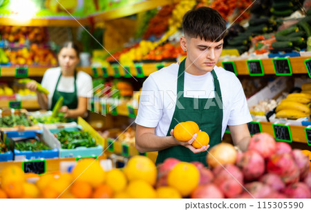 Man store employee displaying assortment of oranges at fruit department in supermarket Man store employee displaying assortment of oranges at fruit department in supermarket 115305590