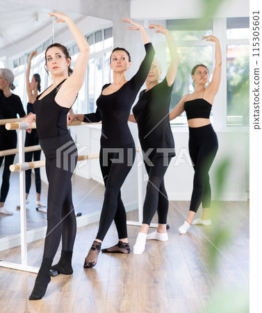 Female ballet trainer teaching group of dancers near ballet barre in dancing studio Female ballet trainer teaching group of dancers near ballet barre in dancing studio 115305601